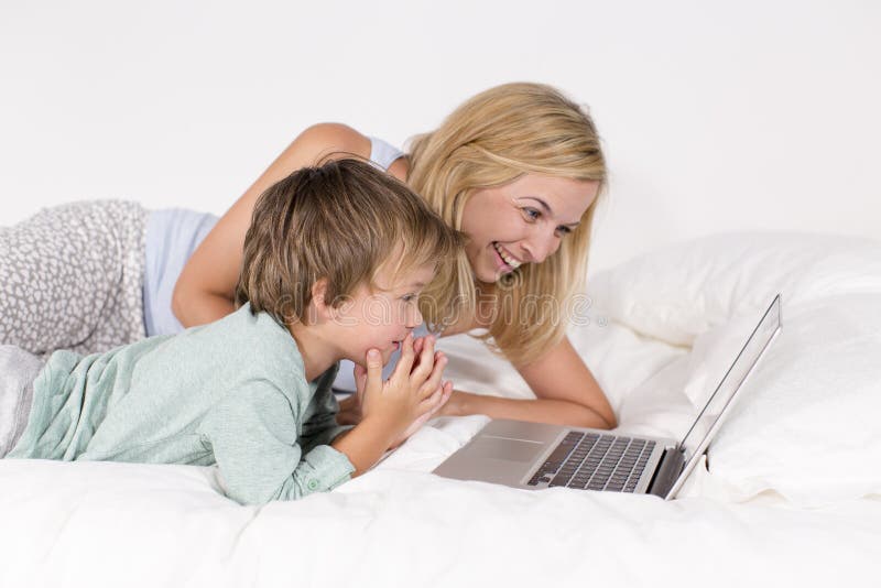 Mother and son lie with notebook on a bed. 