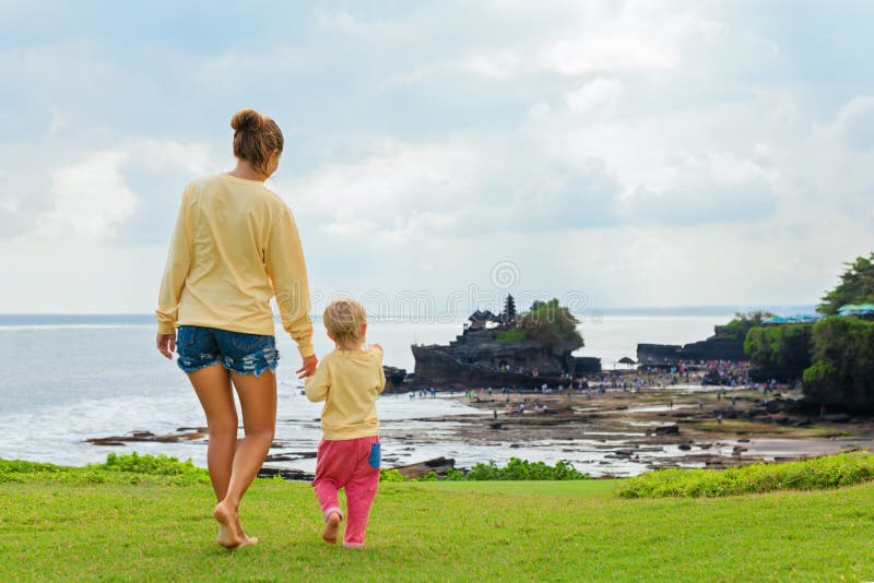 Happy child at walk with parent. Mother, baby son look from high cliff at beach, Balinese temple Tanah lot. People activity on summer tropic holiday with kid on Bali island. Family travel lifestyle. Happy child at walk with parent. Mother, baby son look from high cliff at beach, Balinese temple Tanah lot. People activity on summer tropic holiday with kid on Bali island. Family travel lifestyle.