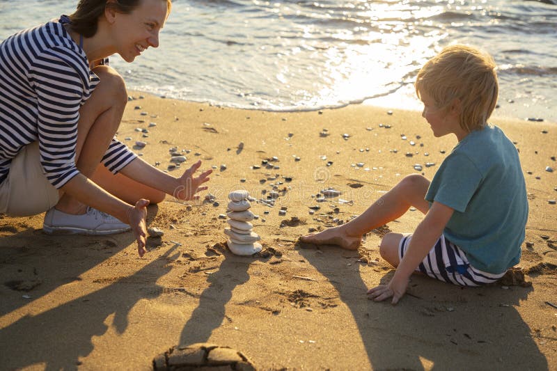 mother and son play with stones building a tower on the beach on a sunny day