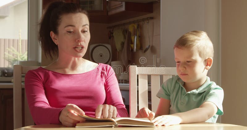 Mother and Son Reading a Book Together Sitting at the Table with Sunshine