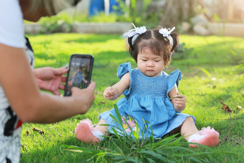 Mother taking a photo with her baby daughter sitting on yard.