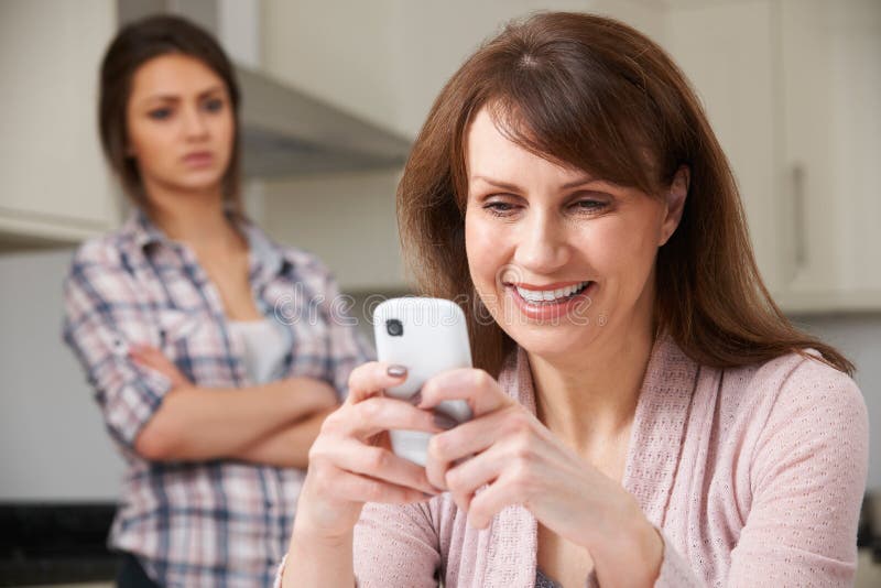 Mother Texts On Mobile Phone As Daughter Watches In Background stock photography Mother Texts On Mobile Phone As Daughter Watches In Background stock photography