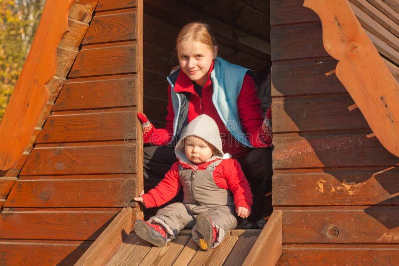 Mother and toddler girl sit in small house on pla