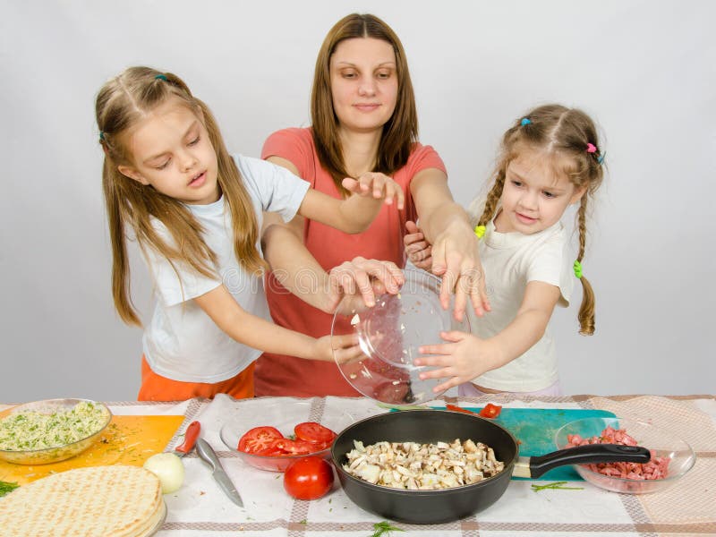 Mother with two daughters at kitchen table with a plate of mushrooms is poured into the pan royalty free stock images Mother with two daughters at kitchen table with a plate of mushrooms is poured into the pan royalty free stock images