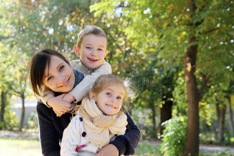 Mother and two kids hugging in autumn park