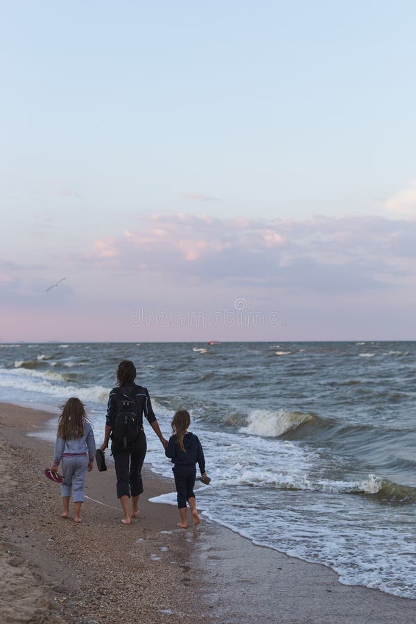 Mother with two little daughters walks along the beach at sunset stock image Mother with two little daughters walks along the beach at sunset stock image