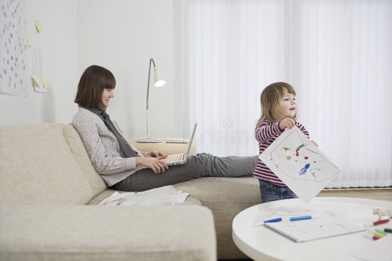 Mother Using Laptop And Daughter Drawing At Home royalty free stock photo Mother Using Laptop And Daughter Drawing At Home royalty free stock photo