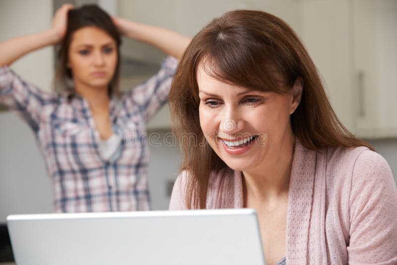 Mother Using Laptop With Frustrated Daughter In Background royalty free stock image Mother Using Laptop With Frustrated Daughter In Background royalty free stock image