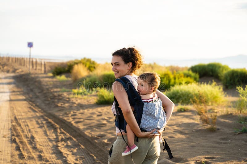 Mother Walking while Carrying a Baby on Her Back in a Baby Carrier