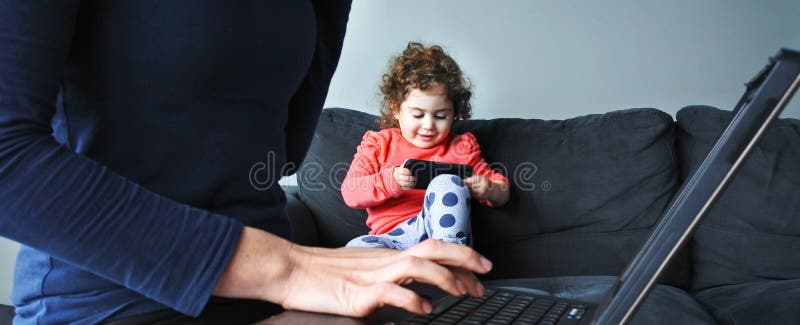 Mother works on laptop while her child plays on smartphone royalty free stock images Mother works on laptop while her child plays on smartphone royalty free stock images