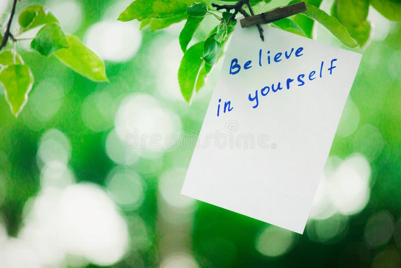 Motivating phrase Believe in yourself. On a green background on a branch is a white paper with a motivating phrase. royalty free stock images