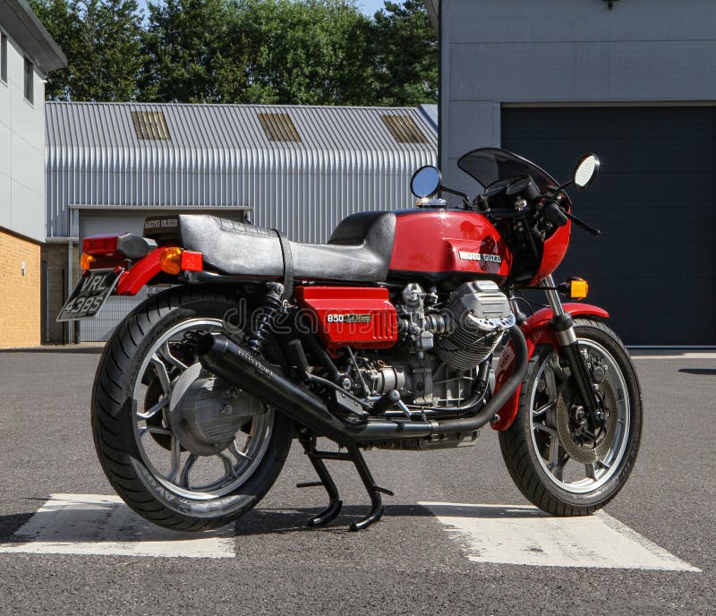 Moto Guzzi 850cc Le Mans Mk1 - Red. Front view. Shows clearly 90 degree transverse V twin engine. Headlight on. Sitting on white pedestrian crossing with an Industrial warehouse backdrop. Moto Guzzi 850cc Le Mans Mk1 - Red. Front view. Shows clearly 90 degree transverse V twin engine. Headlight on. Sitting on white pedestrian crossing with an Industrial warehouse backdrop.