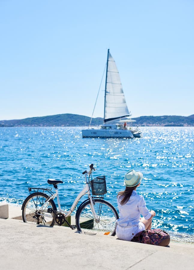 Motociclista turistico della giovane donna con la bicicletta della città nella città vicino al mare immagini stock Motociclista turistico della giovane donna con la bicicletta della città nella città vicino al mare immagini stock