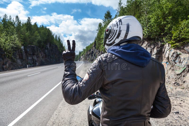 Motocyklu kierowcy tylni widok przy asfaltową drogą siedzi na motocyklu i pokazuje zwycięstwu szyldową dowcip rękę