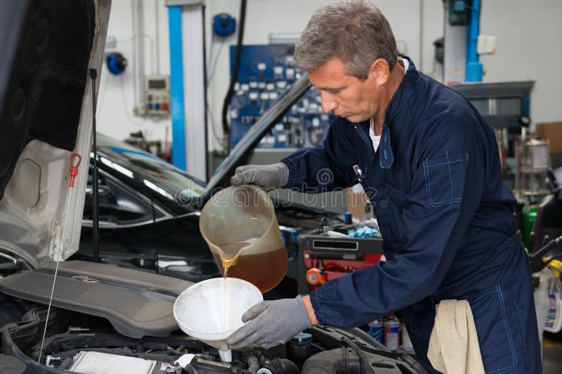 Mechanic Pouring Oil Into Car Engine At Workshop. Mechanic Pouring Oil Into Car Engine At Workshop