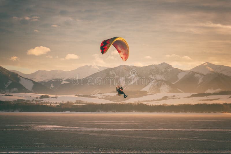 Paragliding over the lake with mountains and sky on background, winter sunset landscape, Liptovska Mara, Slovakia