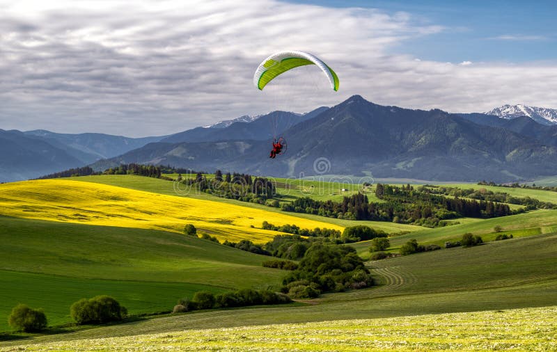 Motorový paragliding přes zelená zemědělská pole a hory v krásné zemi