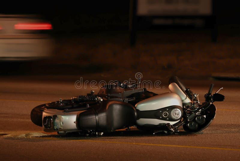 Motorcycle lying on side in street with car speeding by in the background. Motorcycle lying on side in street with car speeding by in the background.