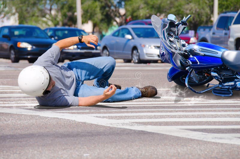 Motocyklový jazdec má stroskotala a leží v ceste, ako jeho motocykli ide posuvné do rušnej križovatke.