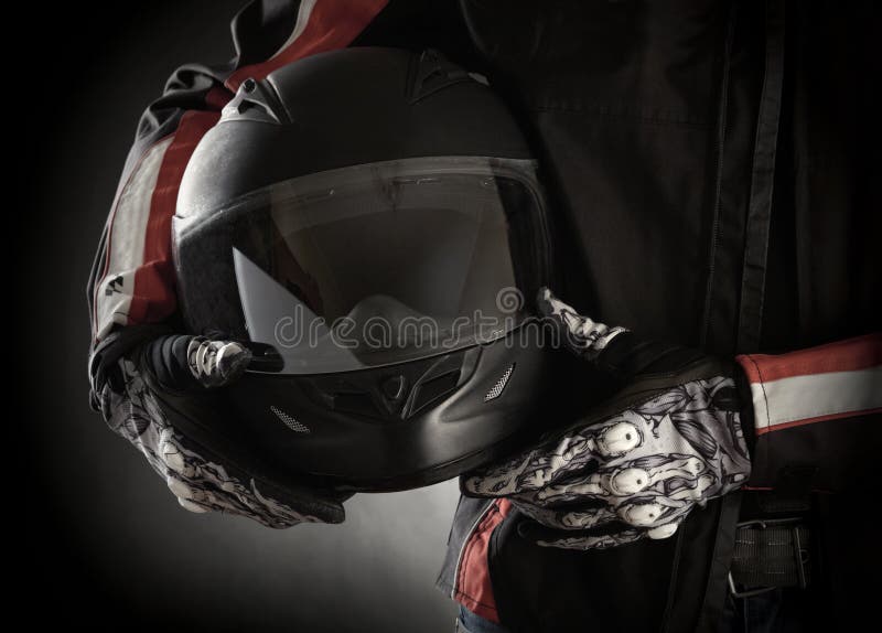 Motorcyclist with helmet in his hands. Dark background