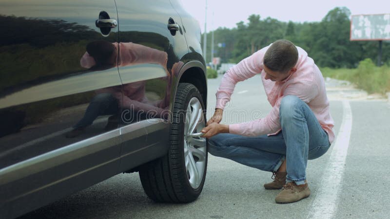 Motorista masculino que desaparafusa a roda de carro pela chave na estrada