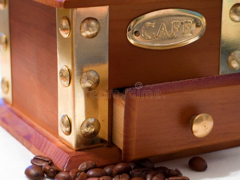 A close up shot of a coffee mill with coffee beans scattered next to it on the table. A close up shot of a coffee mill with coffee beans scattered next to it on the table.