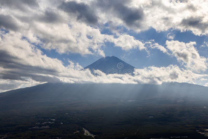 Mount Fuji surrounded by drifting clouds with sun rays piercing through creating a dramatic and mystical atmosphere royalty free stock image