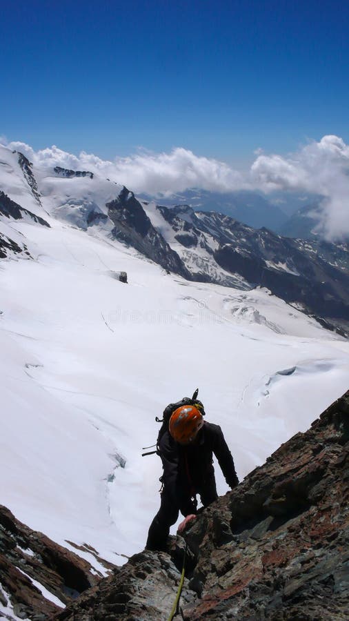 Mountain climber in silhouette climbing a steep rocky mountain peak high above white and wild glaciers with a great view behind hi stock image Mountain climber in silhouette climbing a steep rocky mountain peak high above white and wild glaciers with a great view behind hi stock image
