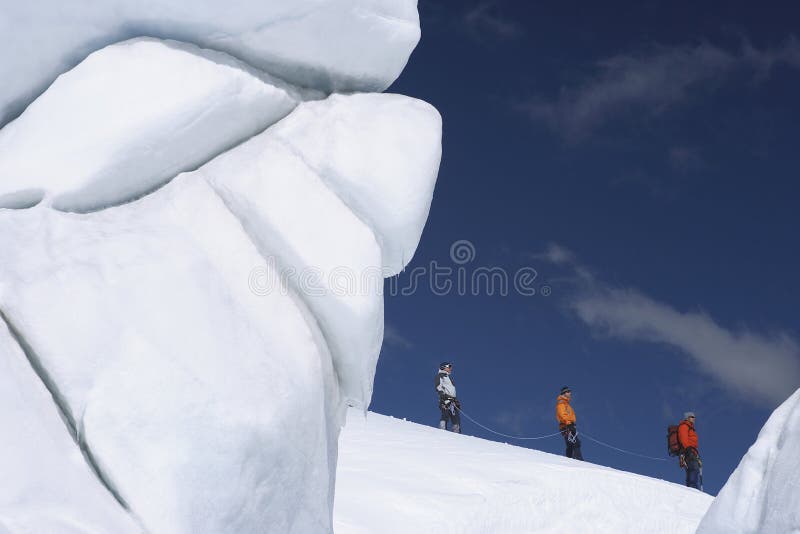 Side view of three hikers walking past ice formation at a distance in snowy mountains. Side view of three hikers walking past ice formation at a distance in snowy mountains