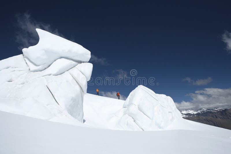 Side view of two hikers walking past ice formations at a distance in snowy mountain. Side view of two hikers walking past ice formations at a distance in snowy mountain