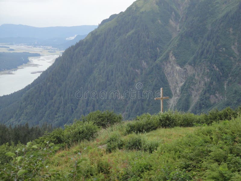 Cross on Mountain Range with Forests and Stream. Lush temperate rainforest in alaska with clouds and sun stock image Cross on Mountain Range with Forests and Stream. Lush temperate rainforest in alaska with clouds and sun stock image