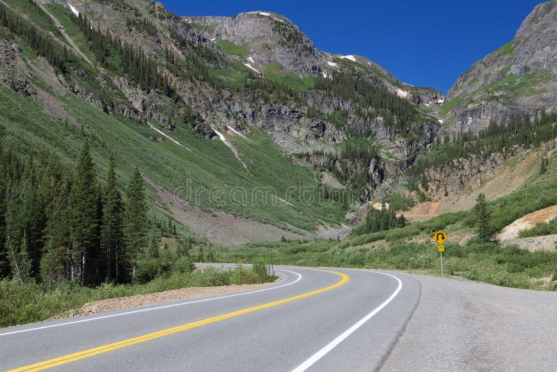Mountain road curves in front of large mountains in Colorado. Paved mountain road curves left in front of high green and rocky mountain peaks in Colorado stock photo Mountain road curves in front of large mountains in Colorado. Paved mountain road curves left in front of high green and rocky mountain peaks in Colorado stock photo