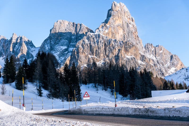 Mountain road overlooked by a towering rocky peak covered in snow in winter