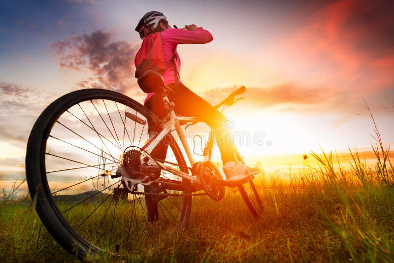 Women cyclists mountainbike is drinking water on the meadow at sunset, Silhouette of cyclist in motion. Women cyclists mountainbike is drinking water on the meadow at sunset, Silhouette of cyclist in motion