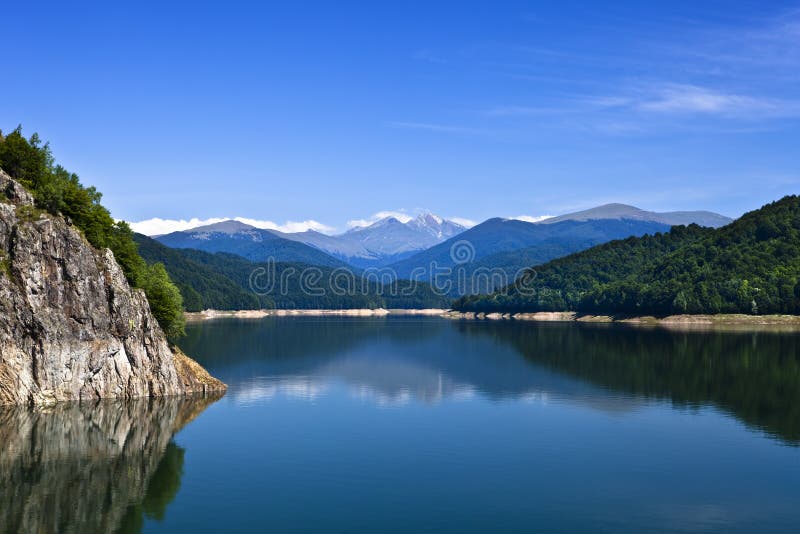 Montagne che si riflettono in un calmo lago di acqua e di cielo blu e chiaro.