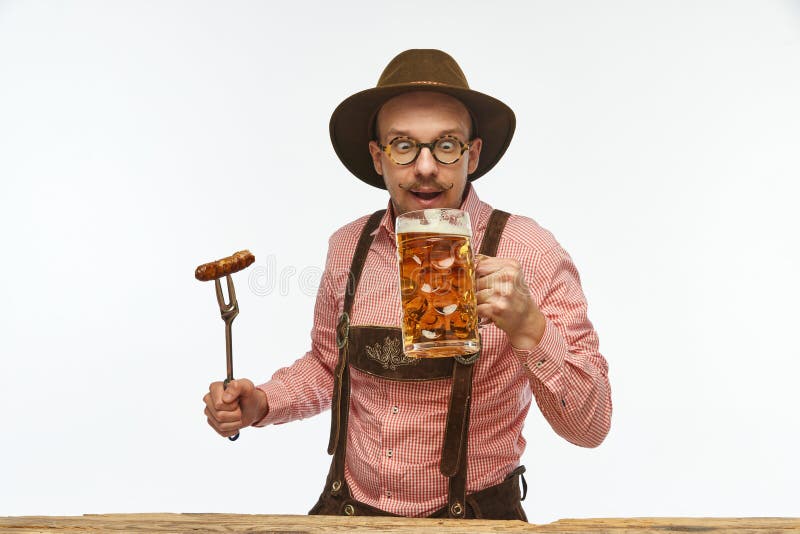 Bavarian mustache man wearing traditional fest outfit holding hot fried sausage and looking at huge glass of beer. Concept of Oktoberfest, traditions, drinks and food. Copy space for ad. Bavarian mustache man wearing traditional fest outfit holding hot fried sausage and looking at huge glass of beer. Concept of Oktoberfest, traditions, drinks and food. Copy space for ad