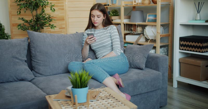 Mouvement lent d'une jeune femme au visage sérieux utilisant un smartphone à la maison sur un canapé banque de vidéos