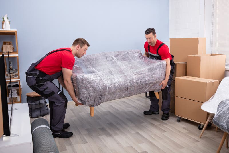 Movers masculinos carregando sofá embrulhado em casa nova