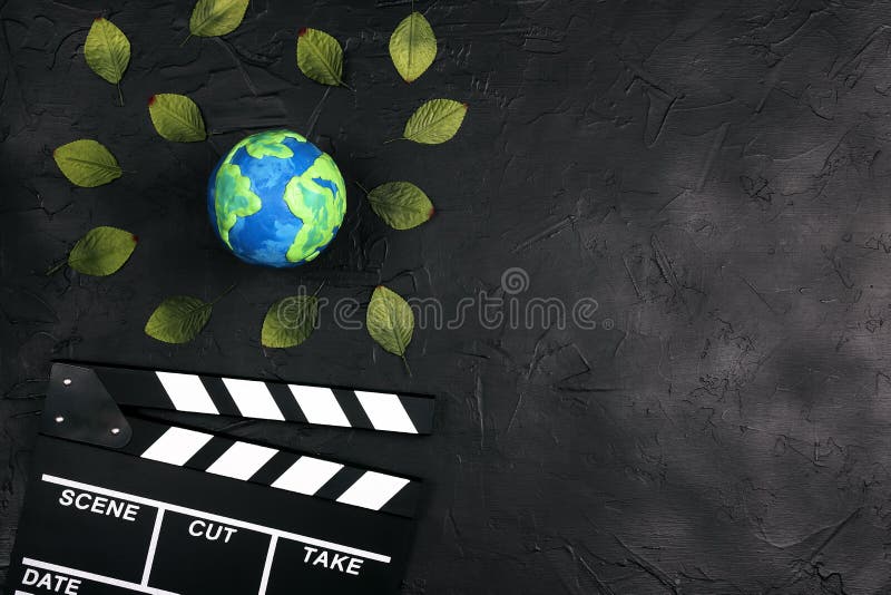 Movie clapper board and globe surrounded by leaves on black background