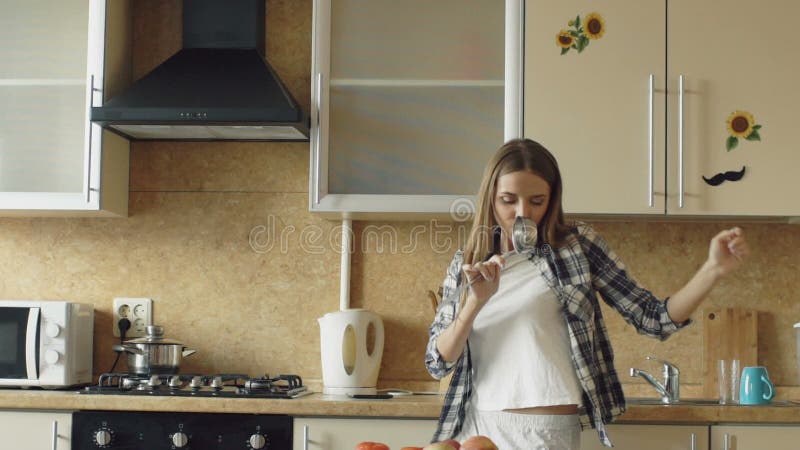 Movimento lento da dança engraçada nova alegre da mulher e canto com concha quando ao cozinhar na cozinha