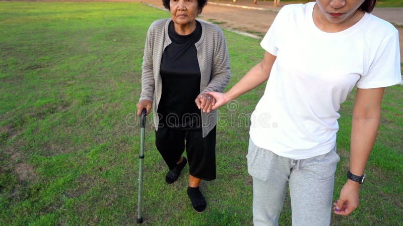 Movimento lento de mulher segura mãos de idosa e caminha no parque