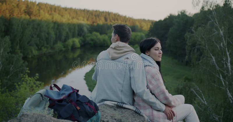 Movimiento lento de hombre y mujer pareja casada sentada en la roca en el bosque de montaña viendo el río disfrutando de paz y tra