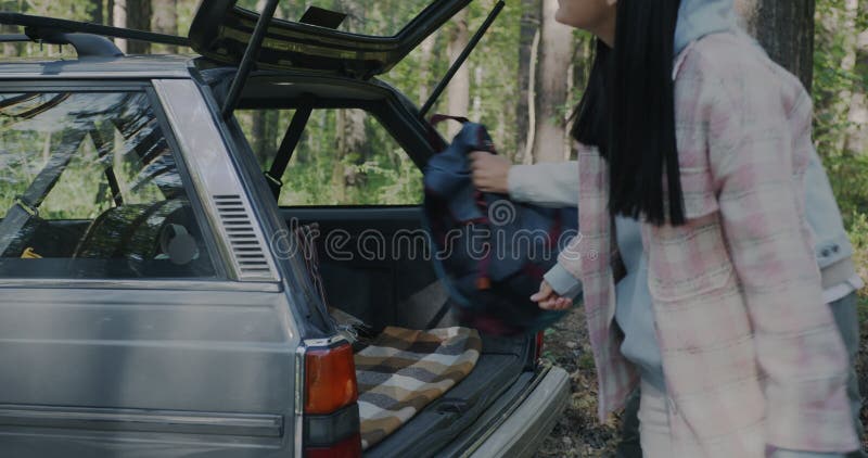 Movimiento lento de hombres y mujeres turistas poniendo mochilas en el maletero de auto al aire libre en el bosque