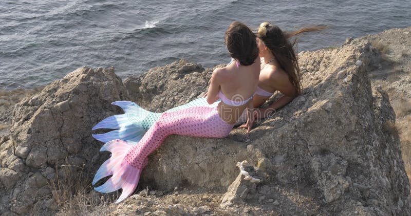 Movimiento lento de mujeres adultas jóvenes con trajes de sirena rosa y azul contra el fondo del mar azul