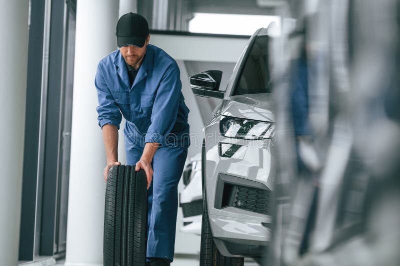 Moving the Tire. Man in Blue Uniform is Working in the Car Service