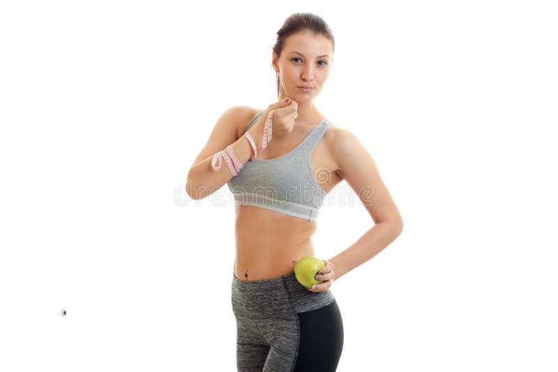 Beautiful young girl in grey top looks at the camera and holding a measuring tape and Apple isolated on white background. Beautiful young girl in grey top looks at the camera and holding a measuring tape and Apple isolated on white background