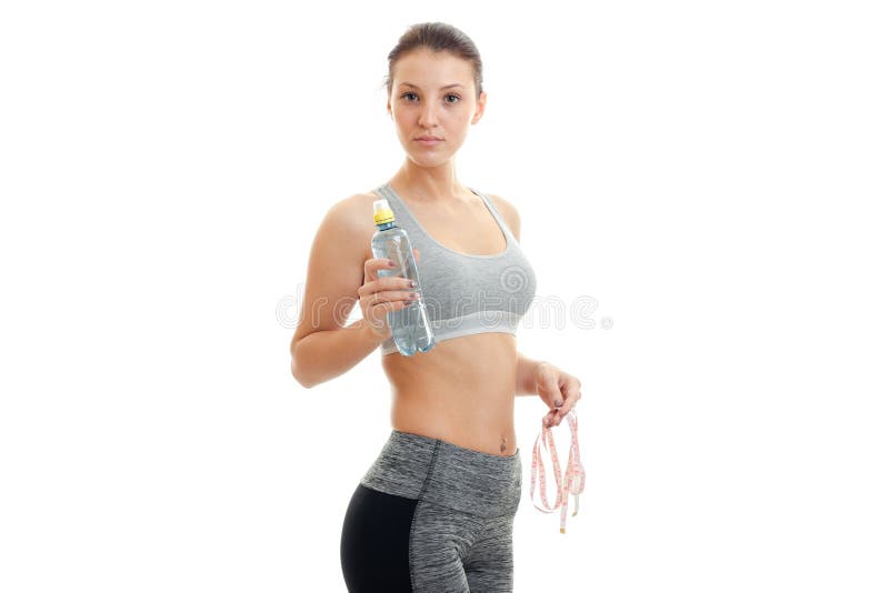 Cute young girl in grey top looks at the camera and holding a water bottle isolated on white background. Cute young girl in grey top looks at the camera and holding a water bottle isolated on white background