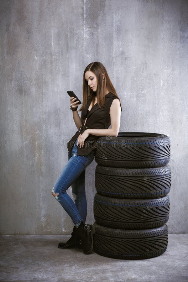 A moça com um telefone celular, está inclinando-se contra os pneus sobre imagens de stock A moça com um telefone celular, está inclinando-se contra os pneus sobre imagens de stock