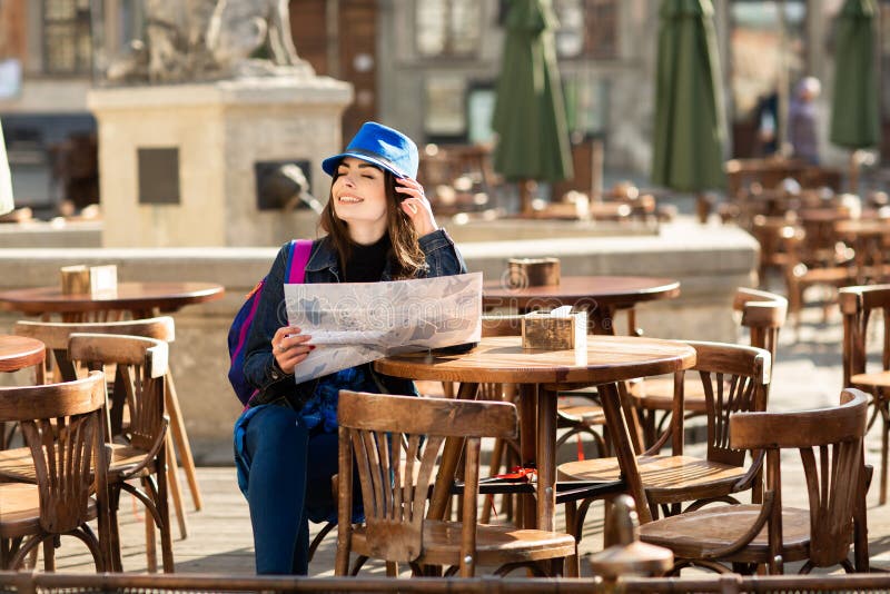 Moça em um chapéu azul que descansa no terraço do verão na cidade velha, e olhando o mapa Lviv, Ucr?nia foto de stock Moça em um chapéu azul que descansa no terraço do verão na cidade velha, e olhando o mapa Lviv, Ucr?nia foto de stock