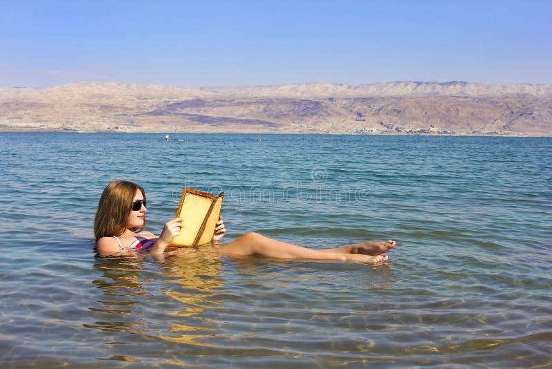 A moça lê um livro que flutua no Mar Morto em Israel
